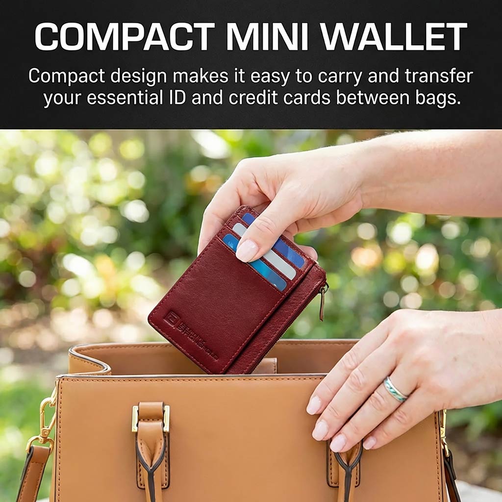 Compact red mini wallet being used to transfer cards between handbags with a blurred outdoor background.